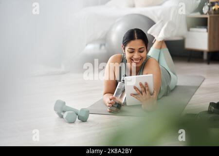 Checking out whats new on her favourite fitness blogs. a sporty young woman using a digital tablet while exercising at home. Stock Photo