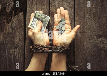 in one hand dollars in the other hand Ukrainian pennies in hands tied with a rope on a wooden table Stock Photo