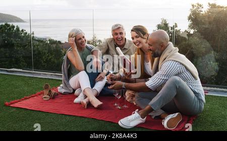 Break open the bubbly, bring on the smiles. two happy couples sitting together and having a picnic outside while drinking champagne. Stock Photo