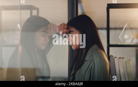 In a panic about her looming deadlines. a young businesswoman looking stressed out in an office at night. Stock Photo