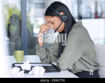 My brain needs a break. a young call centre agent looking stressed out while working in an office. Stock Photo