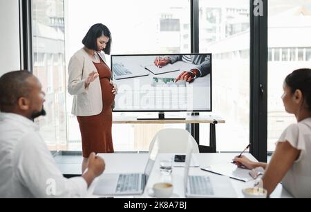 Lets take a break for butterfly kicks. a pregnant young businesswoman delivering a presentation to her team in a modern office. Stock Photo