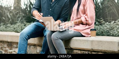 The key to success is to focus on goals not obstacles. two unrecognizable students using a laptop while sitting outside on campus. Stock Photo