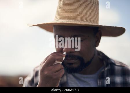 When spring comes around, allergies go up. a mature man using nasal spray while working on a farm. Stock Photo