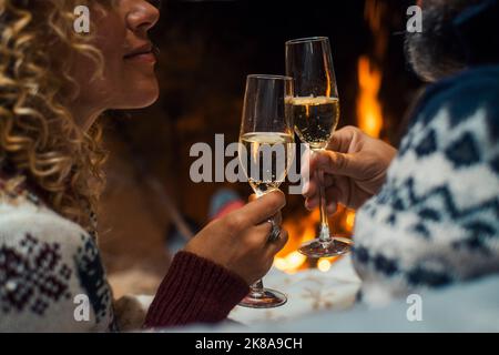 Close up of couple in love clinking with champagne flutes during christmas holiday celebration. Fireplace in background. Winter holidays eve with roma Stock Photo