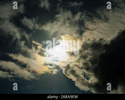 The sun shines through overcast dark yellow-grey storm clouds Stock Photo