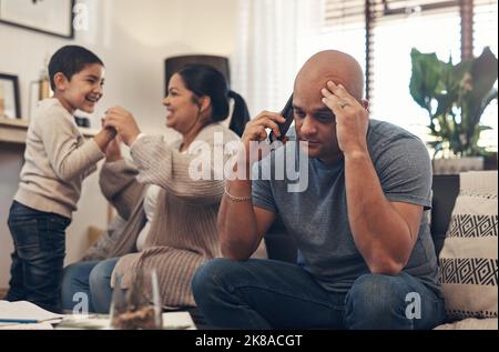 Wheres a game of hide and seek when you need one. a man using a smartphone and looking stressed while his wife and son play together in the background Stock Photo