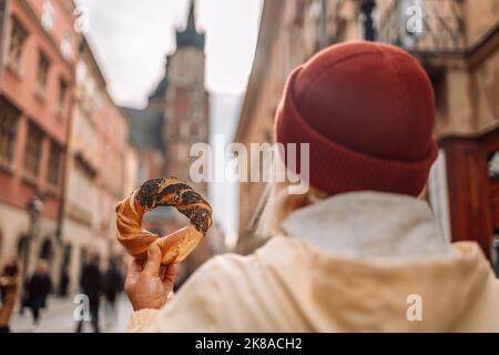 Tourist woman holding bagel prezel obwarzanek traditional polish cuisine snack on Market square in Krakow, Europe  Stock Photo