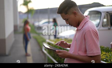 One hispanic man standing outdoors using tablet. South American Brazilian person looking at modern device screen 2 Stock Photo