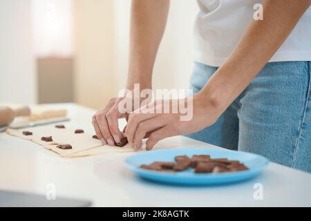 Woman putting chocolate inside rolled out dough on kitchen table Stock Photo