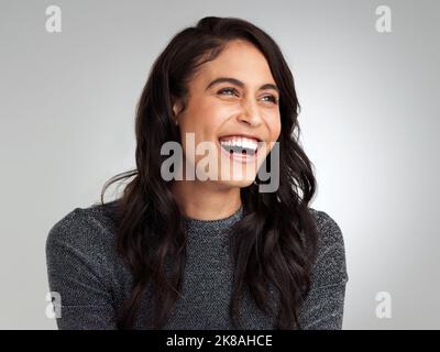 Focus on what makes you happy. a beautiful young woman laughing while standing against a grey background. Stock Photo