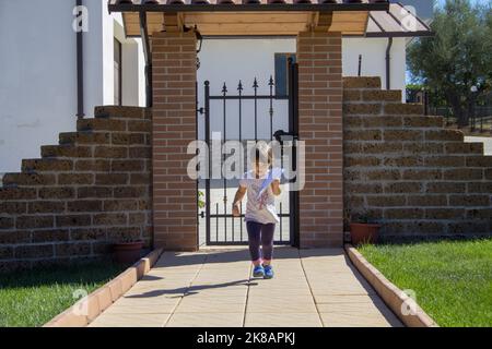 Adorable little girl running in the driveway while playing how to fly a paper airplane. Outdoor games Stock Photo