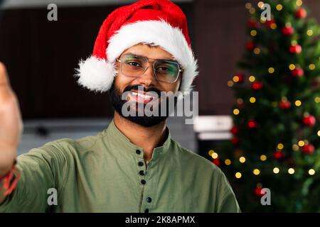 Happy young man wearing santa hat looking at camera celebrating New Year distance online party Stock Photo