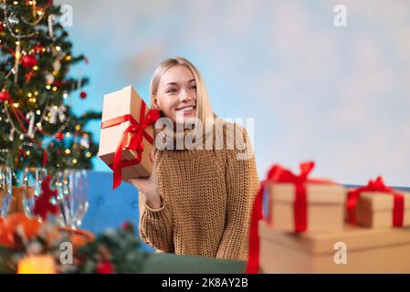 Beautiful girl in a sweater with a New Year's gift in her hands. Photo of an adorable beautiful attractive cute cute girl showing you her wrapped pres Stock Photo