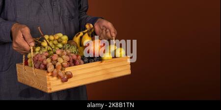 Farmer holding mix fruits basket in hand with banner copy space. Stock Photo
