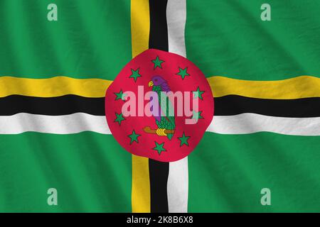 Dominica flag with big folds waving close up under the studio light indoors. The official symbols and colors in fabric banner Stock Photo