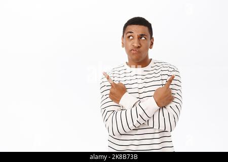 Complicated Black man pointing sideways, showing left and right way, choosing between two products, standing over white background Stock Photo