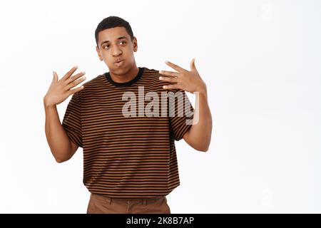 Image of African ameircan man waving at himself, feeling hot, standing over white background Stock Photo