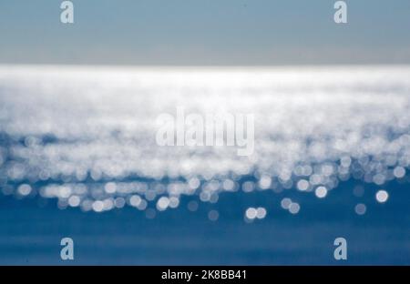 Abstract blurred background.Spots of white reflections of shining sun on blue surface of sea waves.Sea on sunny day.Natural blurry bokeh texture backdrop.Seamless looping.Beautiful natural background Stock Photo