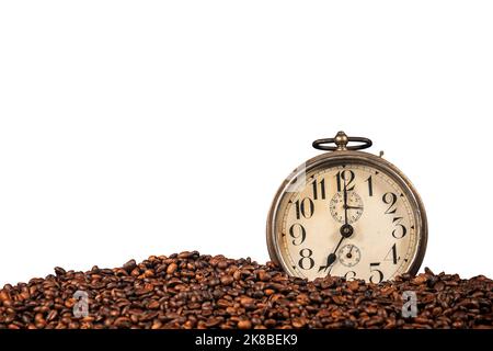 Closeup of an old alarm clock (seven o'clock) and a stack of roasted coffee beans, isolated on white background, photography. Stock Photo