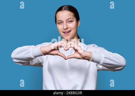 Young teenage female showing heart gesture with hands, on blue background Stock Photo
