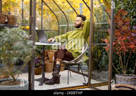 Man works remotely on laptop in glasshouse at backyard Stock Photo