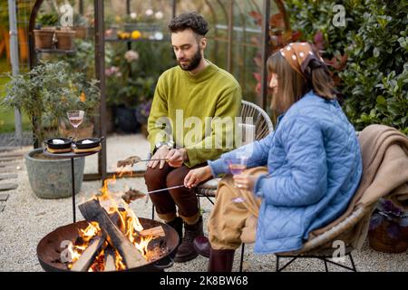 Young couple spending dinner time by the fire at backyard Stock Photo