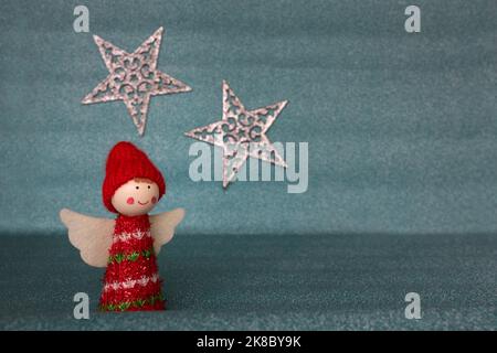 A cute Christmas angel figurine with white wings wearing a red hat and clothes isolated against a glittering pastel blue background with a star Stock Photo
