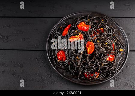Black spaghetti with cherry tomatoes on black boards. Cooked black pasta with red tomatoes on black plate. Top view. Copy space Stock Photo