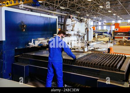 Worker puts steel sheet into loading unit of cutting machine. Stock Photo