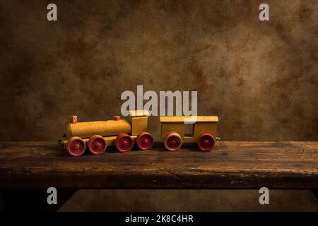 Cute old wooden train toy with red wheels on a rustic old wooden shelf. Stock Photo