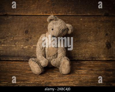 Gray brown little teddy bear on a rustic old wooden shelf. Stock Photo