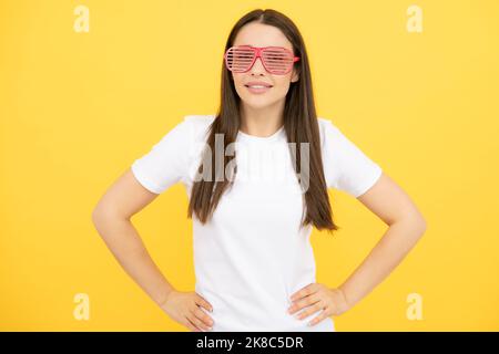 Cheerful girl In large bif funny party glasses sunglasses. Portrait of young woman wearing funny glasses isolated on yellow background. Stock Photo