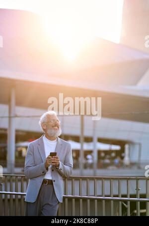 Happy old senior business man using smartphone standing in city outdoors. Stock Photo