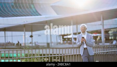Older mature business man using smartphone standing in city outdoors. Stock Photo