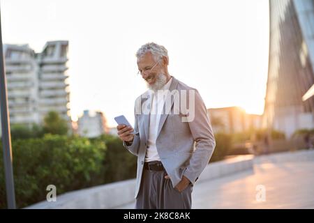 Happy older professional business man holding phone using cellphone outdoor. Stock Photo