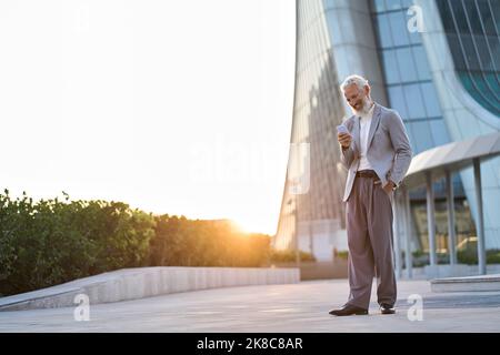 Happy old senior stylish business man holding using mobile phone in city. Stock Photo
