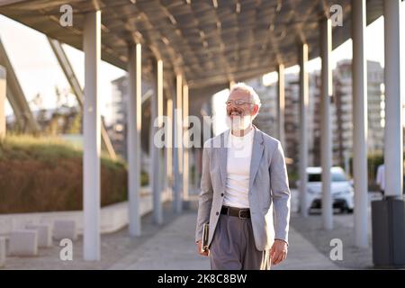 Happy stylish old professional businessman walking outdoors in big city. Stock Photo