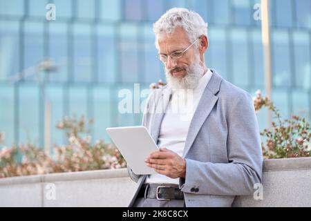Old senior adult professional business man using digital tablet outdoors. Stock Photo