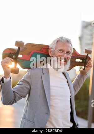 Active happy cool older business man skater holding skateboard in city. Stock Photo