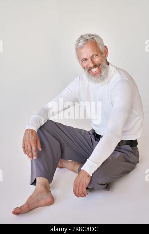 Smiling bearded senior older man sitting on floor at white wall. Stock Photo