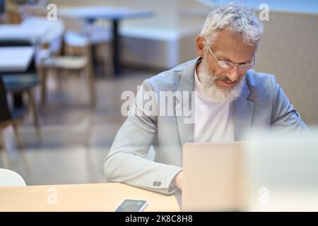 Busy old senior business man office executive using laptop sitting at work desk. Stock Photo