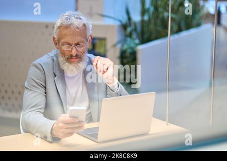 Older senior business man executive using mobile phone working in office. Stock Photo