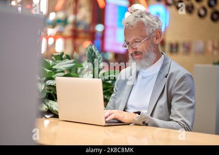 Smiling old senior business man using laptop working late on computer. Stock Photo