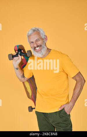 Happy bearded older man skater holding skateboard isolated on yellow. Stock Photo