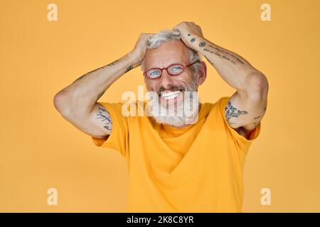 Happy funny older bearded hipster man wearing glasses isolated on yellow. Stock Photo