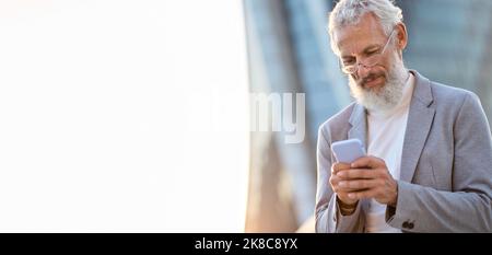 Older mature professional business man holding phone using smartphone outdoor. Stock Photo