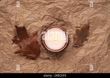 Aroma candle and brown autumn leaves on crumpled paper background. Autumn concept. Top view, flat lay Stock Photo