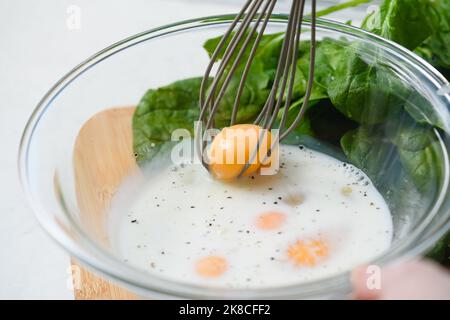 Close-up of a whisk with yolk in a glass bowl. Cooking an omelet. Raw eggs in a bowl with milk and spices. Stock Photo