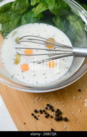 Close-up of a whisk with yolk in a glass bowl. Cooking an omelet. Raw eggs in a bowl with milk and spices. Stock Photo